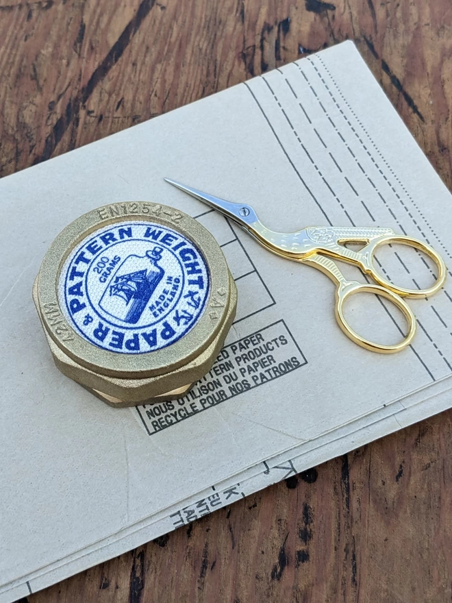 Royal blue pattern and paper weight lying on vintage sewing pattern next to stork embroidery scissors
