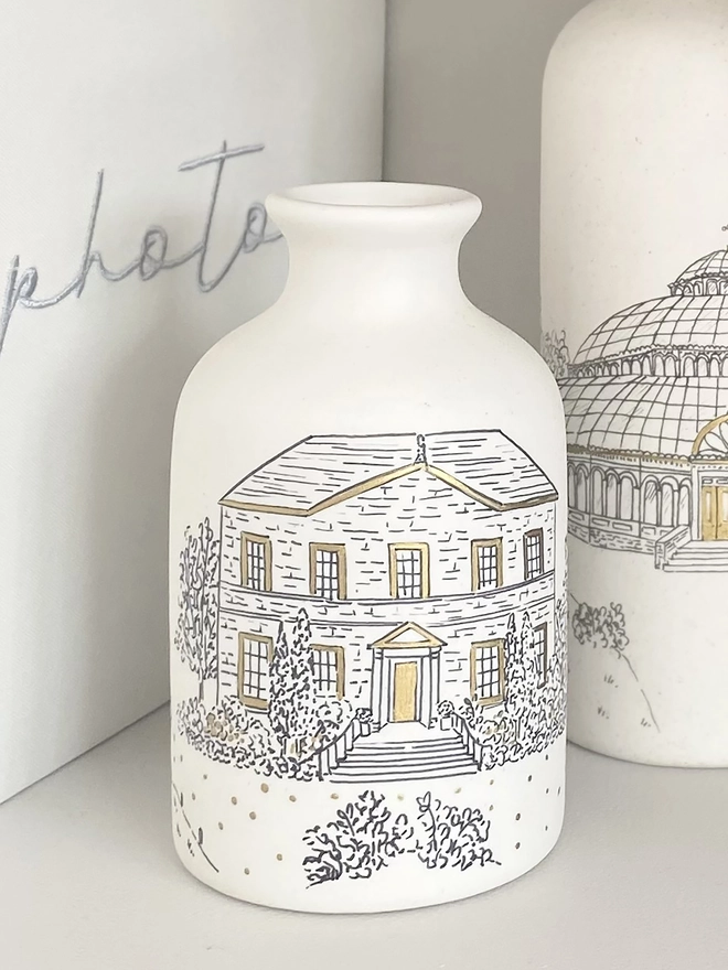 Ceramic vase on a shelf with a black hand drawn venue illustration and hand painted metallic gold highlights