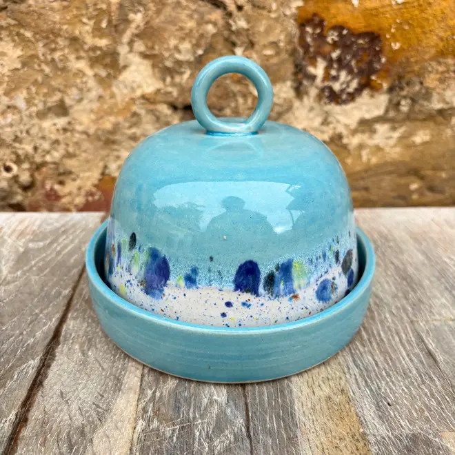 Shoreline Butter Dish, a colourful butter dish placed on a wooden surface against a brick wall. 