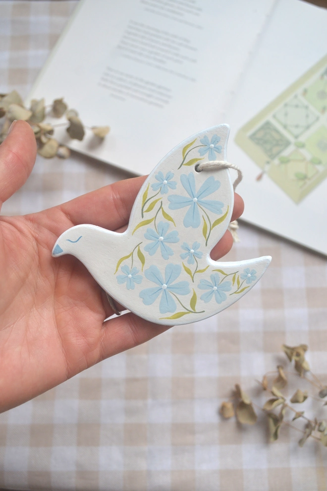 white ceramic hanging bird with blue and green floral designs, in front of gingham 