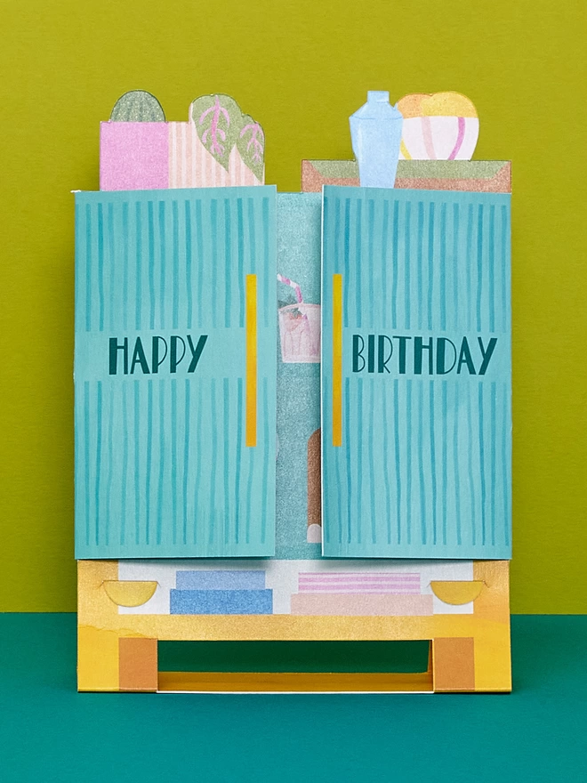 The 3D teal drinks cabinet has both doors closed to show off its hand lettered ‘Happy Birthday' message 