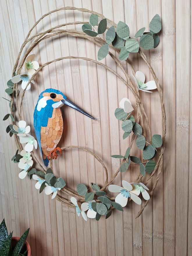 side view of a kingfisher paper sculpture on a floral wreath of peach flowers