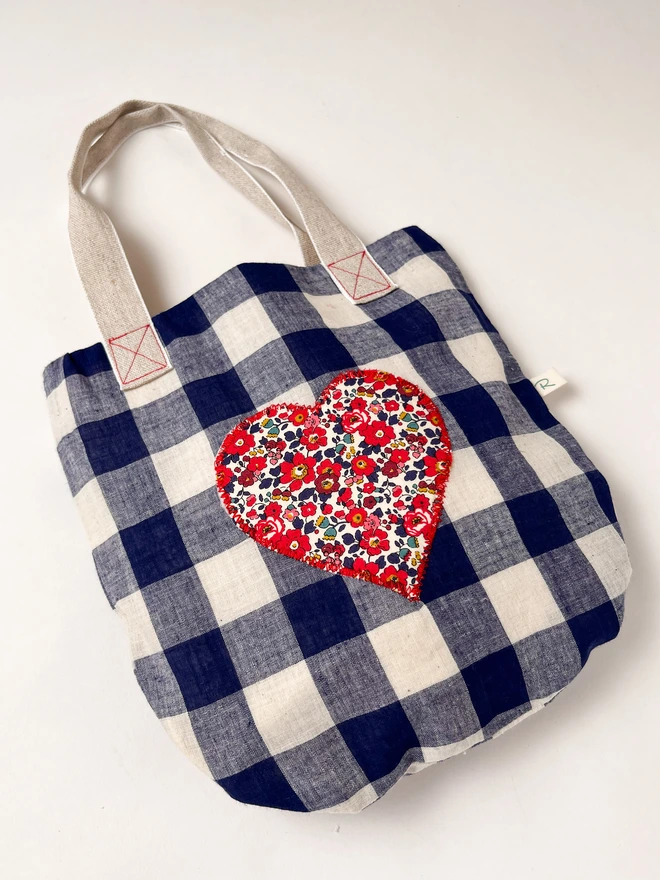 A photo of a blue gingham bag featuring a liberty patch sewn on the front