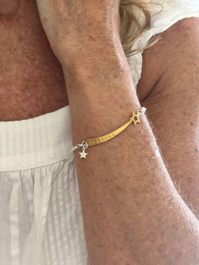 model wears a gold plate shooting star charm on a silver belcher chain bracelet, with small silver mini star