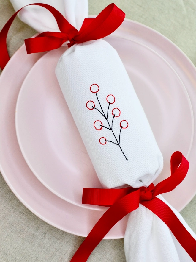 White cotton Christmas cracker with embroidered berry design and red ribbon bows 