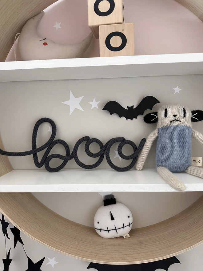 Knitted Wire Word sign: 'boo' with a lowercase b sitting on a shelf in a kid's play room next to some fun and stylish children's decorations. 