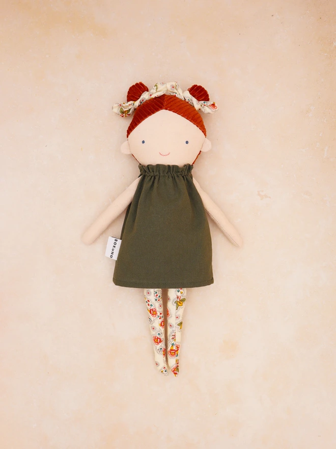 Handmade linen doll with light skin wearing dark green cotton dress and cream floral bows and tights. It has braided red hair made with corduroy.