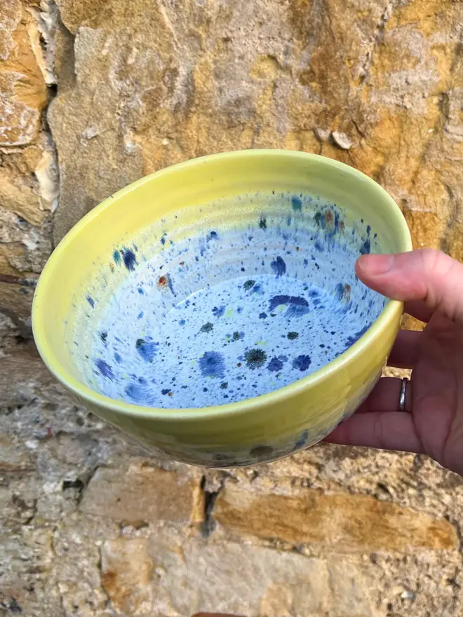 Shoreline Small Bowl, a colourful bowl held in front of a brick wall. 