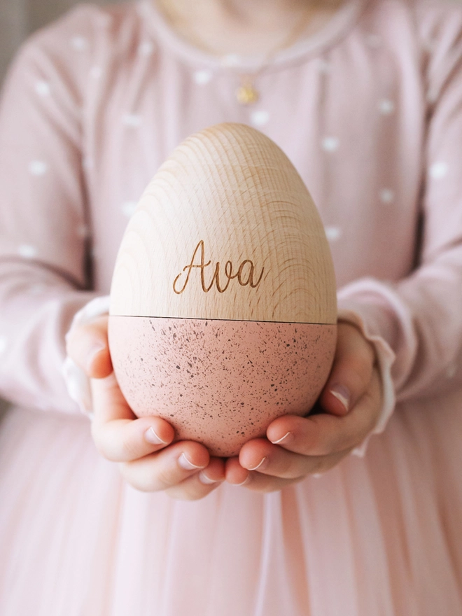 Large fillable wooden egg in the colour salmon, with speckled paint finish engraved with the name Ava.