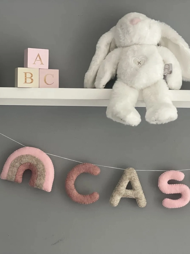 Personalised Name Icon Garland, a child's name banner hanging from a white shelf, nursery decoration, baby gift