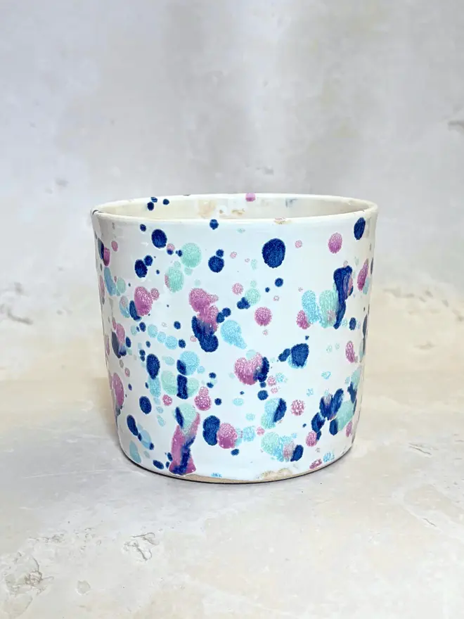 Sweetpea Large Pot, a colourful pot sitting on a stone surface in front of a plain background.