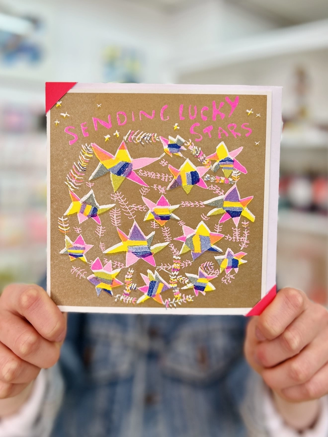 A good luck card with stars in pinks, yellows, blues on gold with the words Sending Lucky Stars