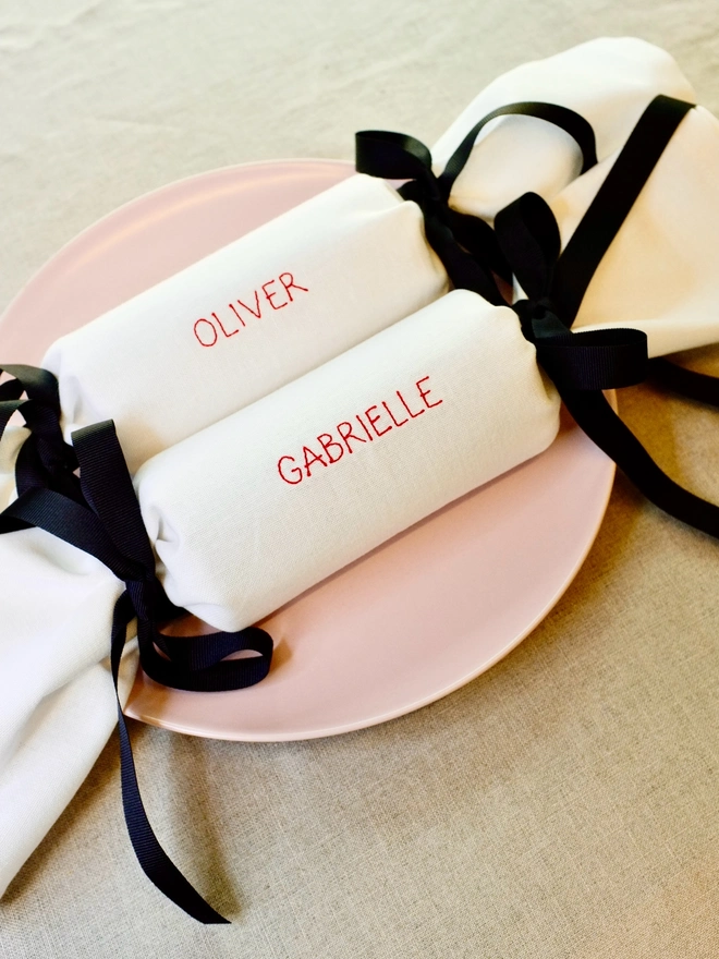 White cotton fabric Christmas cracker napkins personalised with names and black grosgrain ribbon bows