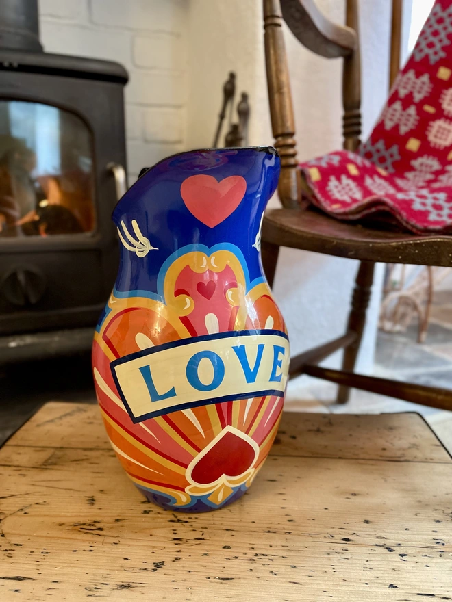 Vintage blue enamel jug hand painted with a fairground inspired design in pink, orange, yellow and red.