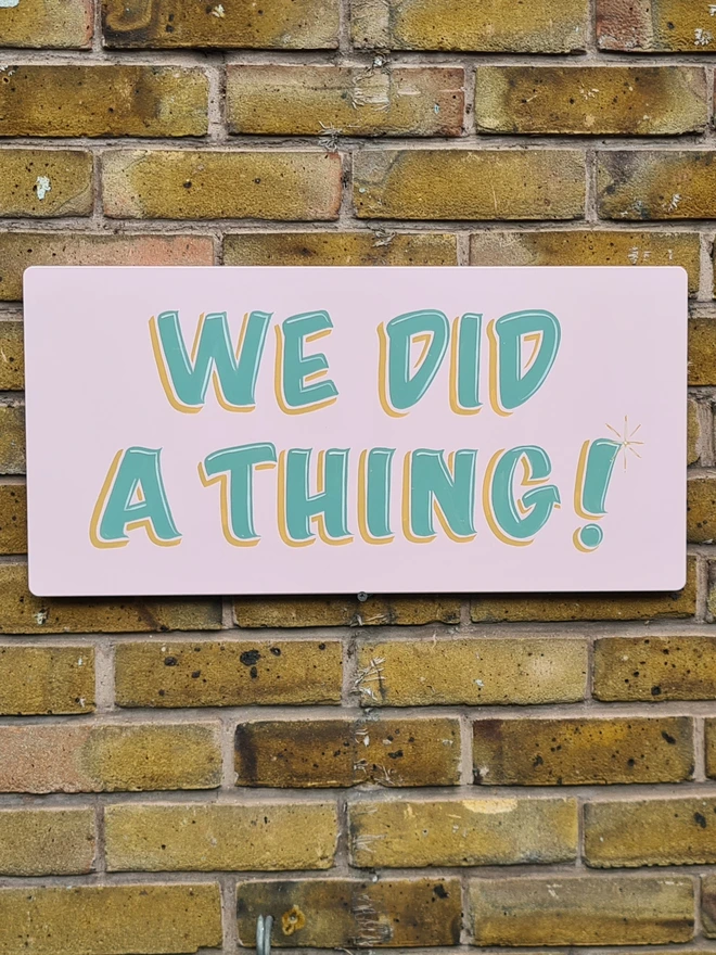 'We Did A Thing' Colourful Wedding Sign, a colourful wedding sign in pink with green text, hung on a brick wall