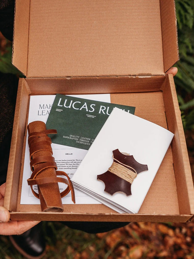 make your own leather journal. an open cardboard box containing components for a DIY leather journal kit.