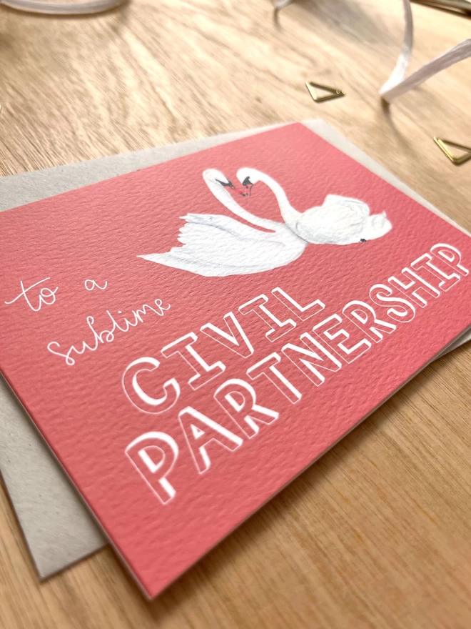 a greetings card with a deep pink background featuring two swans with their necks meeting in a heart shape, and the phrase “to a sublime CIVIL PARTNERSHIP”