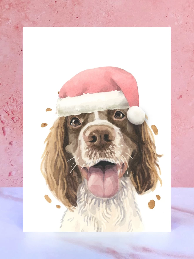 A Christmas card featuring a hand painted design of a springer spaniel, stood upright on a marble surface. 