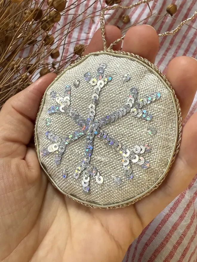 embroidered linen sparkly snowflake decoration. snowflake hanging ornament photographed against pinstripe fabric backdrop.