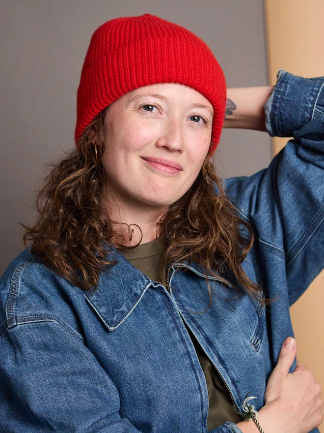 Bright Red Ribbed Beanie Modelled In Front Of A Colourful Background