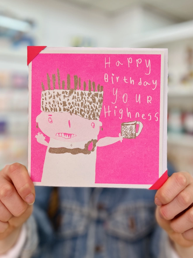 Bright pink with flashes of gold,a riso printed birthday card that says Happy Birthday Your Highness