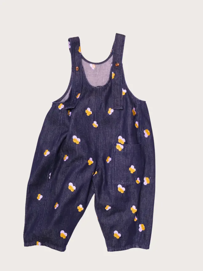 Back flat lay of Studio Koter Kai dungarees in Denim Petal, showing embroidered petals and a flap patch pocket.