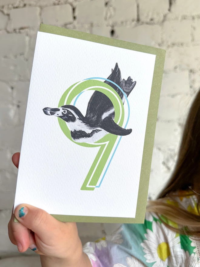 white card with a big green number 9 and a penguin illustration and a green envelope