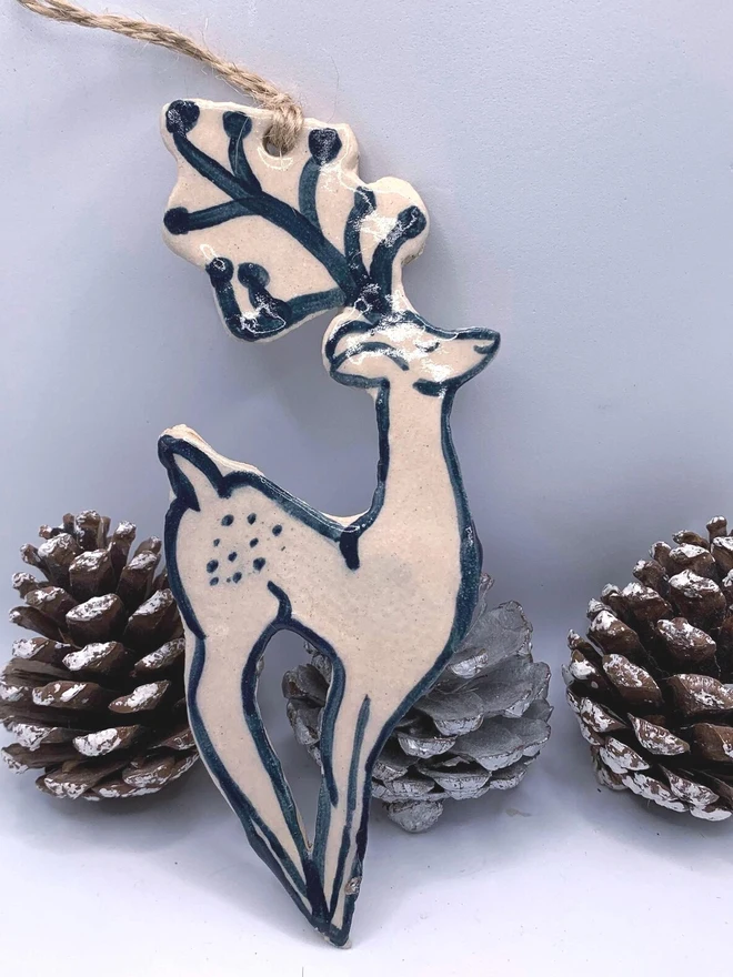 Handmade Ceramic Reindeer Ornament Scandinavian Folk Decor, a colourful reindeer decoration sitting on a plain surface joined by some acorns. 