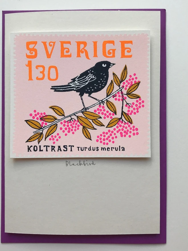 Bird Stamp Card Swedish/ Blackbird, a white card with a colourful bird design on a white backdrop. It sits above a purple envelope. 