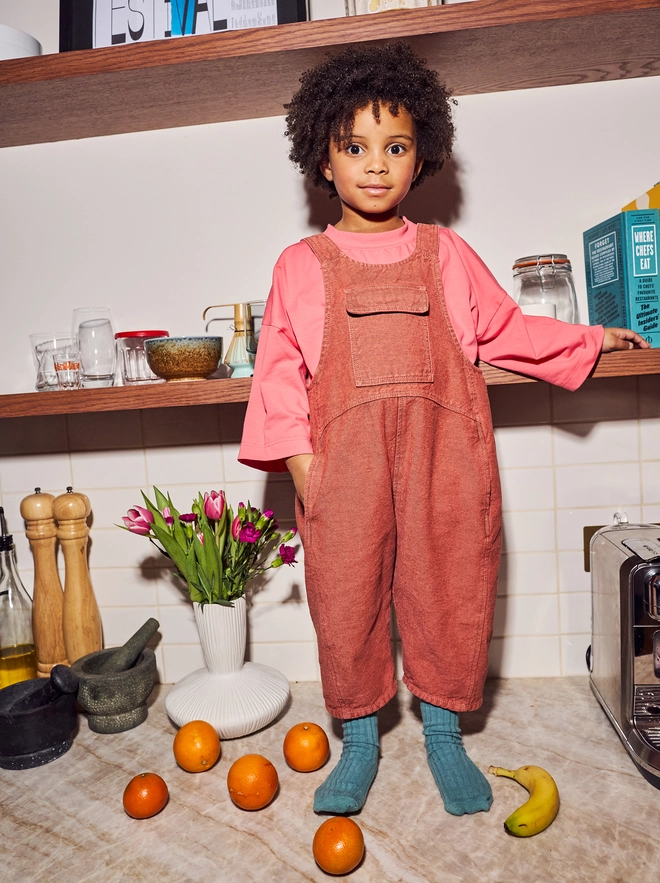 Child wearing oversized denim dungarees playing in a kitchen