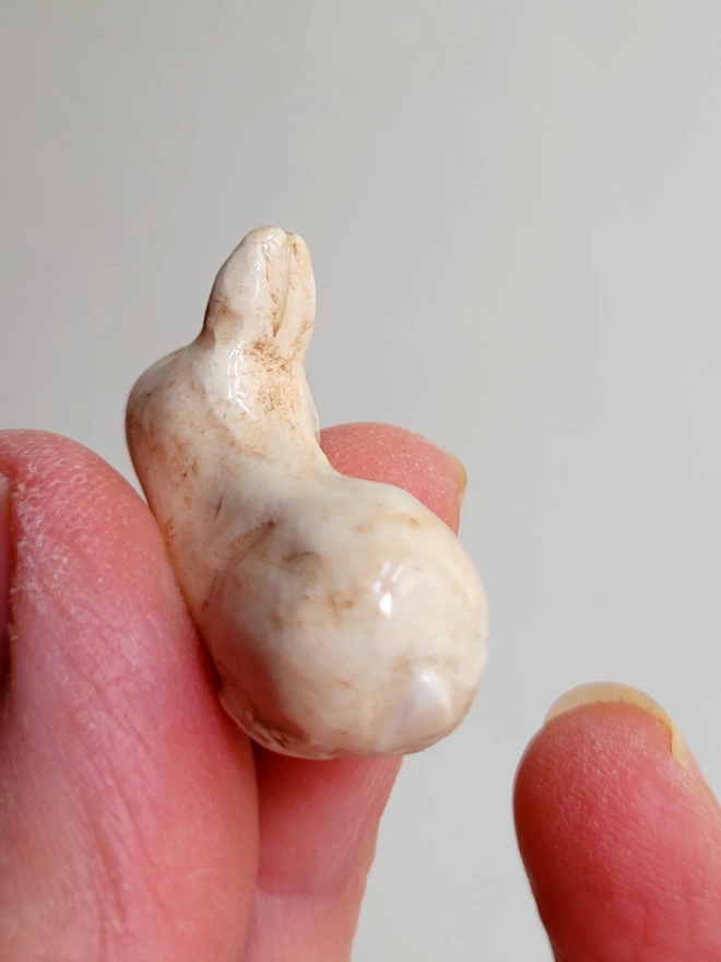 little beige bunny rabbit figure held in a hand showing the back view with a tiny tail