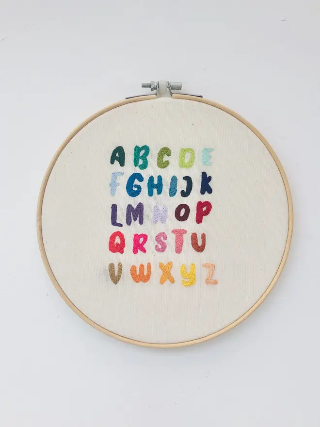 letters of the alphabet embroidered hoop. colourful stitch alphabet hoop on plain white background.