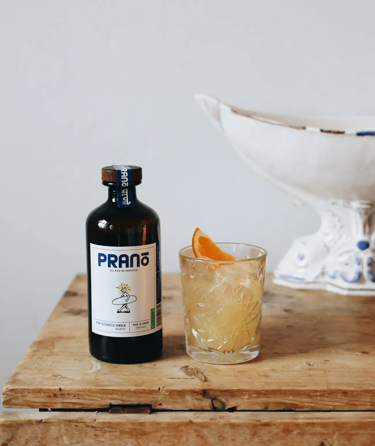 Bottle of prano sitting next to a glass of the pale orange beverage garnished with a slice of orange. Both sitting on a brown countertop with white background 