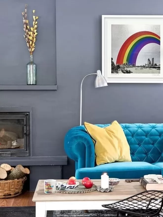 Living room with blue couch and yellow cushion with grey walls and rainbow artwork hung on the wall 