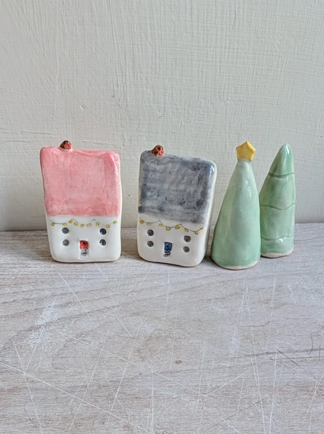 pink and grey tiny pottery house with a tiny robin bird on top of each with 2 ceramic Christmas trees 