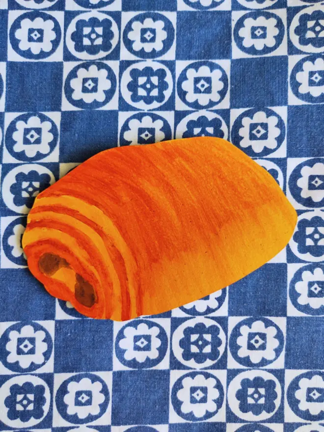 hand painted pain au chocolat, cut out paper shape. on blue and white tablecloth
