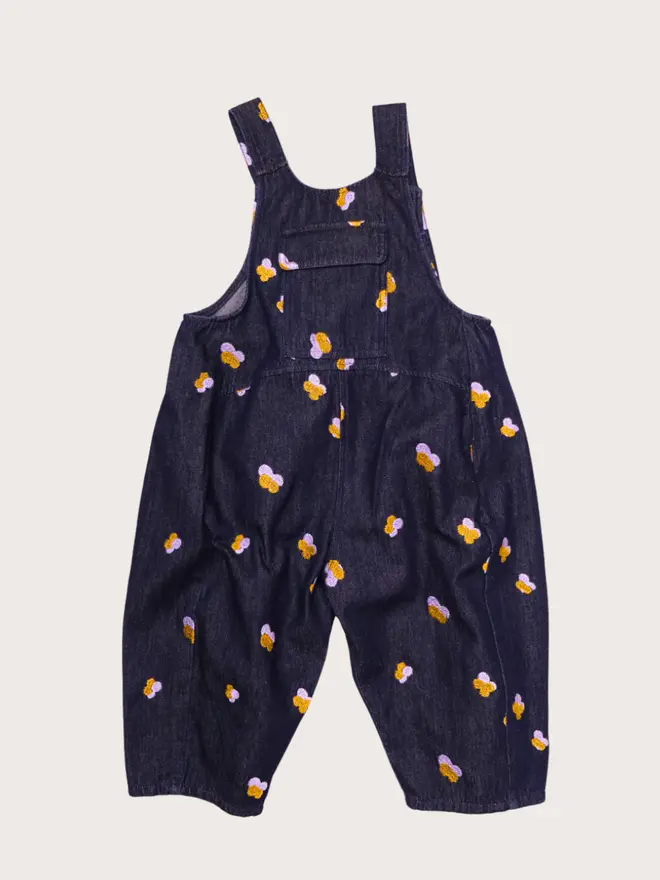 Front flat lay of Studio Koter Kai dungarees in Denim Petal, dark denim with lilac and gold embroidered petals, chest pocket and button straps.