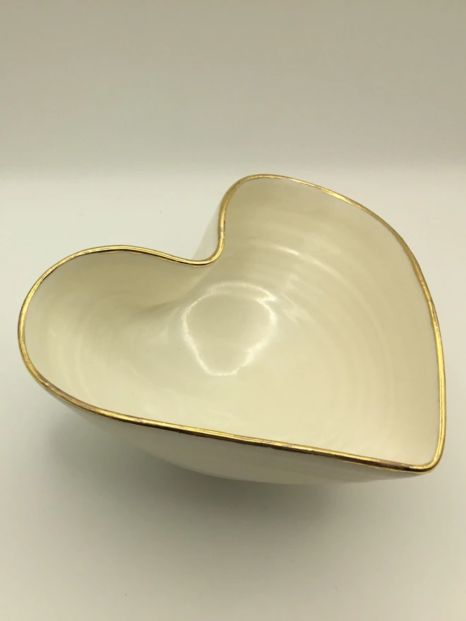 porcelain heart shaped bowl. a white heart shaped bowl with a gold rim, on a white background.