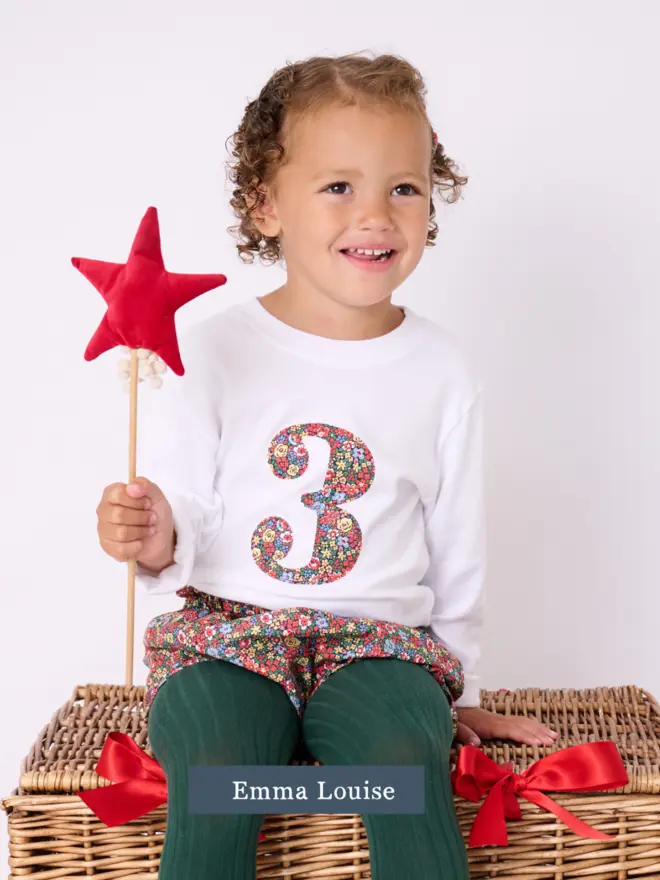a 3 year old girl wearing a white birthday t-shirt with a number 3 cut from liberty floral print on the front