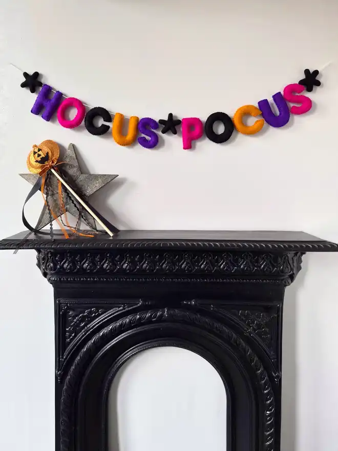 Felt halloween garland featuring the word 'Hocus Pocus', hanging above a fireplace. 
