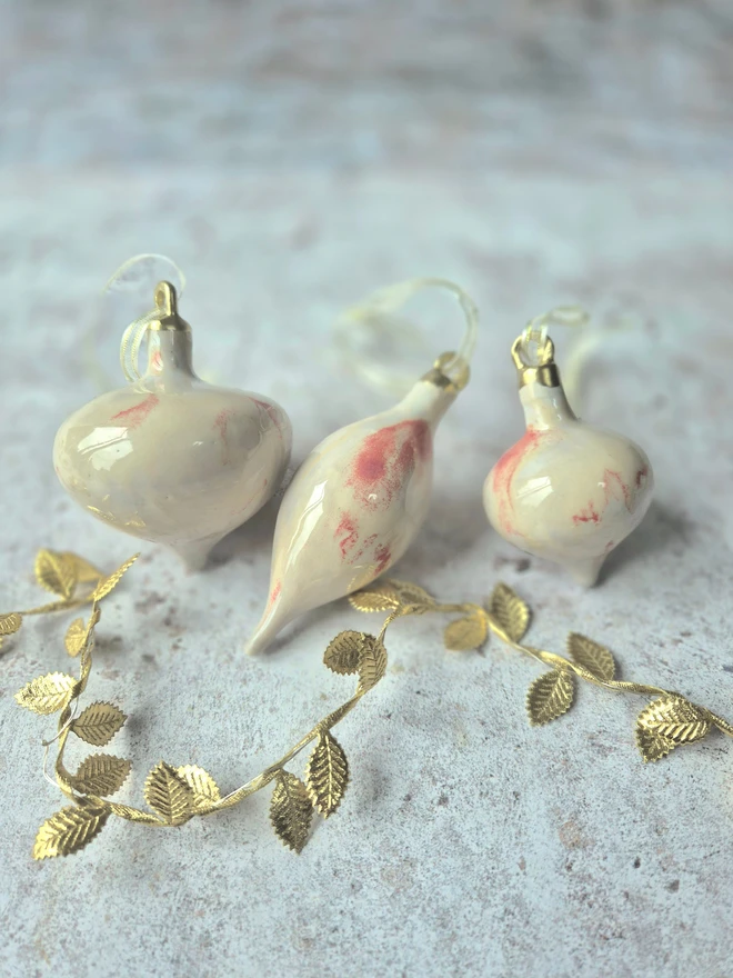 Ceramic christmas bauble decorations in a pearlescent glaze with white, cream and pink and gold, with silk ribbon and gold detailing. Photographed on a pearlescent serving dish with gold pears and christmas lights, gift, christmas, ceramics, pottery, christmas, decorations, christmas tree