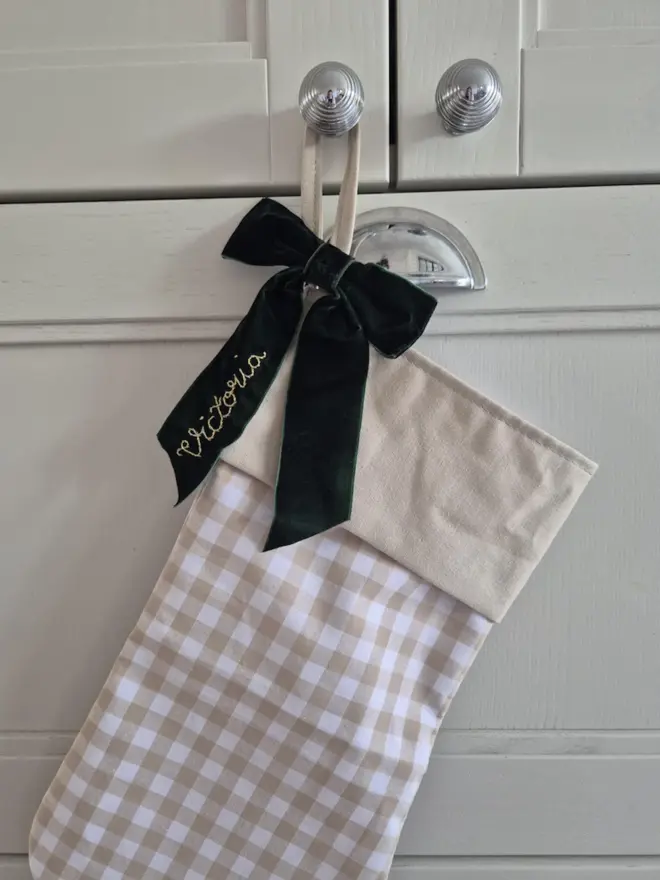 beige gingham stocking with dark green velvet bow, embroidered with a name