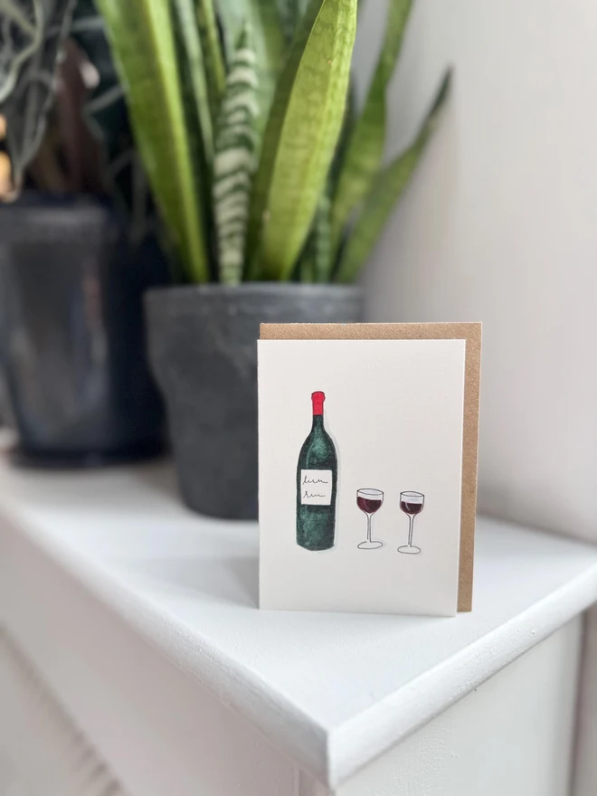 red wine illustrated mini card. card photographed on mantelpiece with houseplants in background.