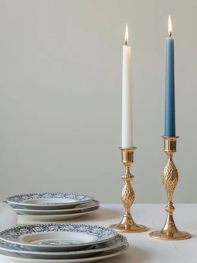 Duck blue dinner candle in a candle holder next to some china plates on a table