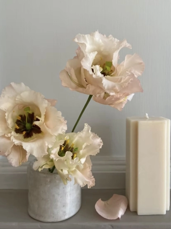 Ikebana, ceramic vase pictured with pink flowers next to a candle. 