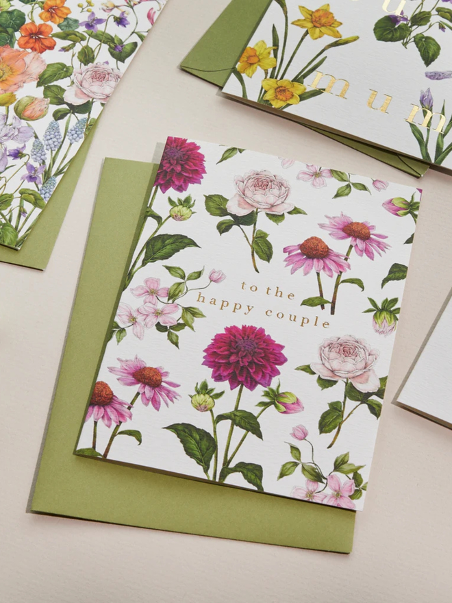 'to the happy couple' illustrated floral card. a white floral card and green envelope photographed against a plain background.
