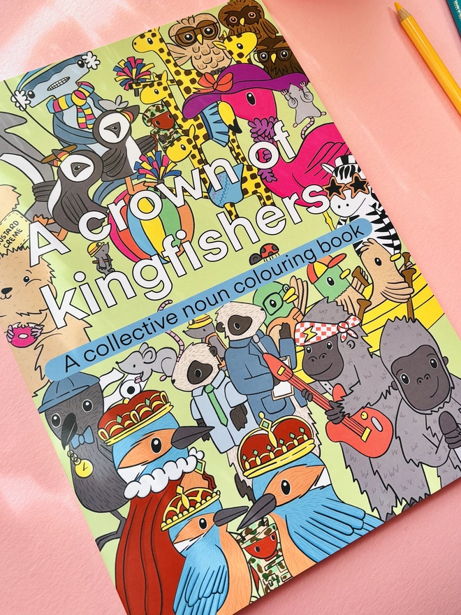 Colouring book title reads “A crown of kingfisher: a collective noun colouring book” and the front cover shows lots of animals from the pages of the colouring book including a band of gorillas, circus of puffins, tower of giraffes