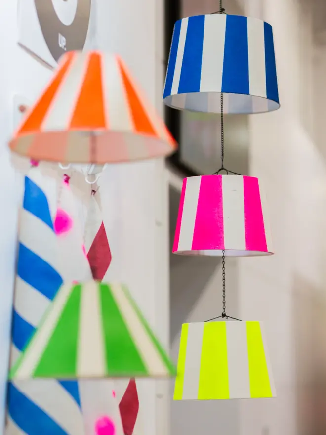 Hand Painted Upcycled Striped Sustainable Drum Lampshade, colourful lampshades hanging in a studio from a string. 