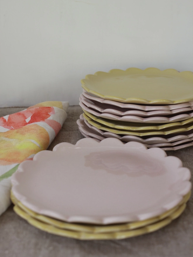 two stacks of camellia scalloped edge side plates in dijon yellow and pale pink