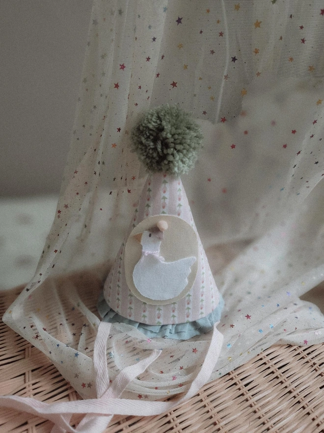 Baby Birthday Hat With Goose, a birthday party hat with a goose. It sits on a wooden hamper. 